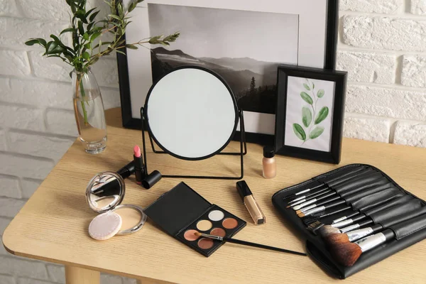 Mirror, makeup products and pictures on wooden dressing table