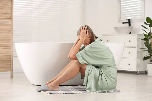 Menopause. Depressed woman near bath tub in bathroom