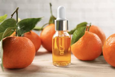 Bir şişe mandalina yağı ve beyaz ahşap masada taze meyveler, yakın plan.