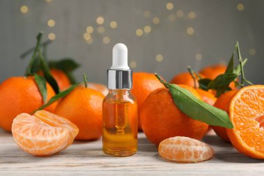 Bir şişe mandalina yağı ve beyaz ahşap masada taze meyveler.