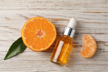 Bir şişe mandalina yağı ve beyaz ahşap masada taze meyve.