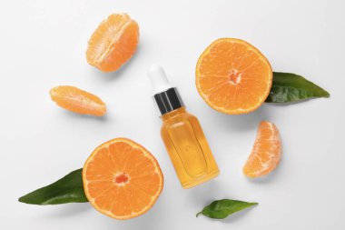 Aromatik mandalina yağı şişede, yapraklar ve narenciye meyveleri beyaz masada, düzdü.