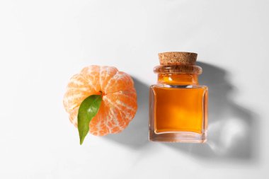 Aromatik mandalina yağı şişede ve turunçgil meyvesi beyaz masada.