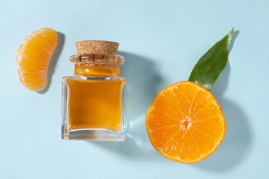 Aromatik mandalina yağı şişede ve narenciye meyvesi açık mavi masada.