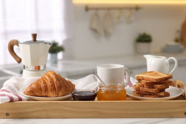 Kahvaltı mutfakta servis edilir. Tost tepsisi, bal, reçel, taze kruvasan, kahve ve sütü beyaz masaya koy, yakın plan.