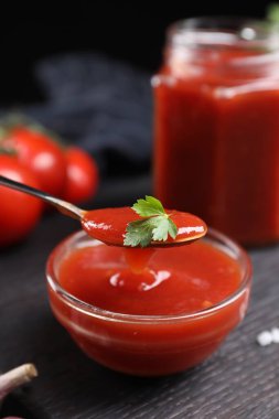 Siyah ahşap masada kaseden kaşıkla lezzetli ketçap alıp yakın plan çekiyoruz. Domates sosu.