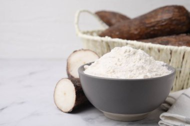 Beyaz mermer masa üzerinde manyok unu ve kökleri olan bir kase. Metin için boşluk