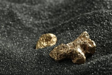 Siyah kumda parlak altın külçeler, yakın plan. Metin için boşluk