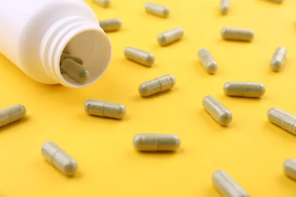 Jar with vitamin capsules on yellow background, closeup