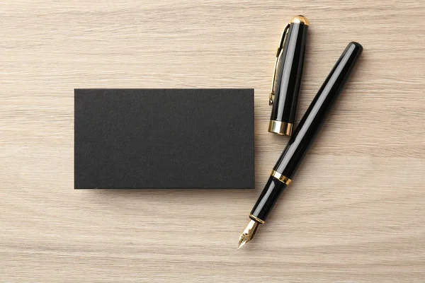 Blank black business card and fountain pen on wooden table, flat lay. Mockup for design