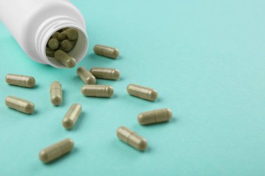 Turkuaz arka planda şişe ve vitamin kapsülleri, yakın plan. Metin için boşluk