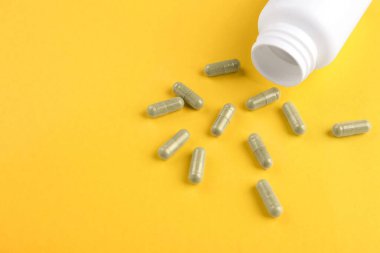 Sarı arka planda şişe ve vitamin kapsülleri, yakın plan. Metin için boşluk
