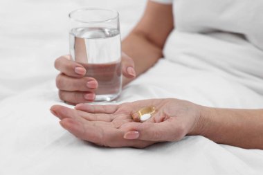 Yatağında vitamin hapları ve bir bardak su olan kadın, yakın plan.