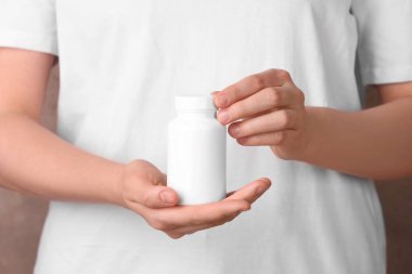 Açık kahverengi arka planda vitamin hapları içeren boş beyaz şişe tutan kadın, yakın plan.
