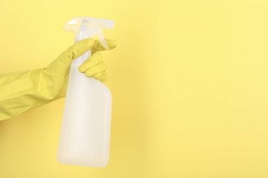 Sarı arka planda plastik sprey şişesi tutan kadın, yakın plan. Metin için boşluk