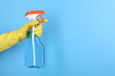 Açık mavi arka planda plastik sprey şişesi tutan kadın, yakın plan. Metin için boşluk