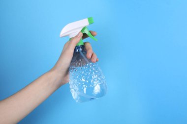 Açık mavi arka planda plastik sprey şişesi tutan kadın, yakın plan. Metin için boşluk