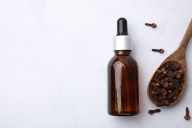 Şişedeki karanfil yağı, beyaz masada kaşık ve kurutulmuş tomurcuklar, üst manzara. Metin için boşluk