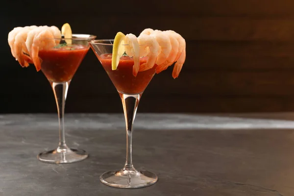 Tasty shrimp cocktail with sauce in glasses and lemon on grey table, space for text