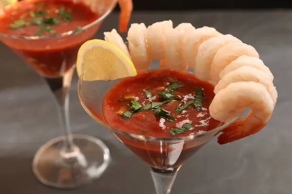 Tasty shrimp cocktail with sauce in glasses and lemon on grey table, closeup