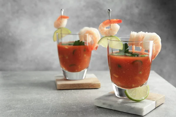 Tasty shrimp cocktail with sauce in glasses and lime on light grey table, space for text