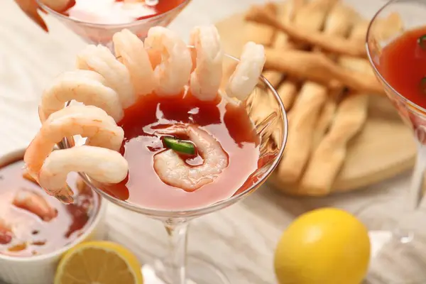 Tasty shrimp cocktail with sauce in glasses and lemon on light wooden table, closeup