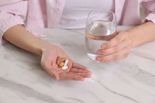 Woman with vitamin pills and glass of water at table indoors, closeup