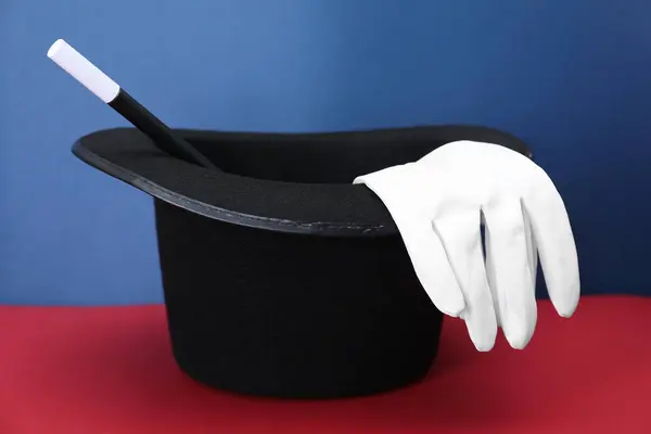 Black top hat, gloves and wand on color background. Magician equipment