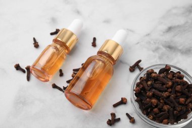 Aromatik karanfil yağı şişelerde ve beyaz mermer masada kurumuş tomurcuklar, yakın plan.