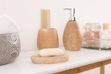 Beyaz duvarın yanındaki masada farklı banyo aksesuarları ve kişisel bakım ürünleri var.