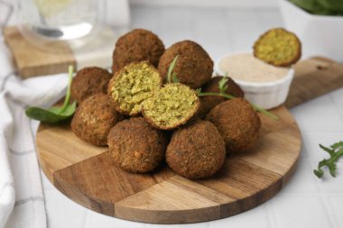 Lezzetli falafel topları, otlar ve soslar beyaz fayanslı masada.