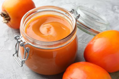 Lezzetli hurma reçeli ve gri masada taze meyveler, yakın plan.