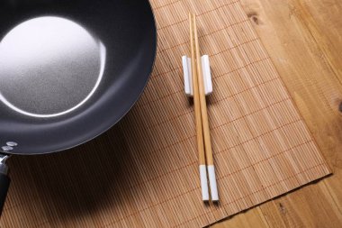 Empty iron wok and chopsticks on wooden table, closeup