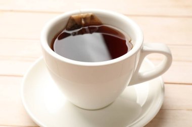 Çay poşeti ve bir fincan sıcak içecek açık ahşap masada, yakın plan.