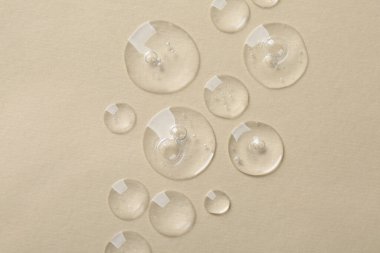 Bej arka planda kozmetik serumu damlaları, üst görünüm