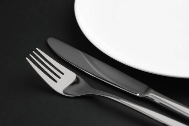 Temiz tabak, çatal ve bıçak siyah masada, yakın plan.
