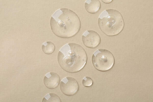 Капли косметической сыворотки на бежевом фоне, вид сверху