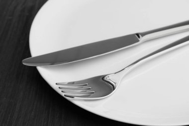 Temiz tabak, çatal ve bıçak siyah tahta masada, yakın plan.