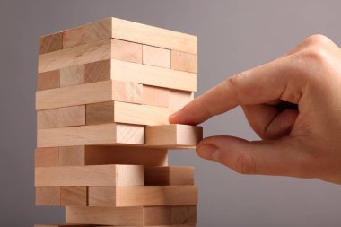 Jenga oynuyorum. Gri arkaplandaki tahta bloğu kuleden kaldıran adam, yakın plan