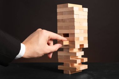 Jenga oynuyorum. Siyah masada, kuleden tahta bloğu kaldıran adam karanlık arka planda, yakın plan.