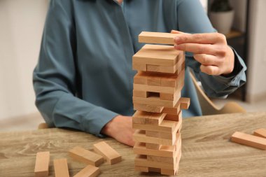 Jenga oynuyorum. Kapalı alandaki ahşap masada blokları olan bir kule inşa eden kadın.