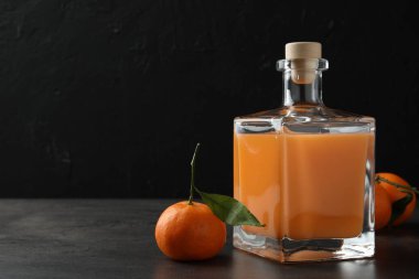Cam şişede nefis mandalina likörü ve gri masada taze meyve, mesaj için yer var.