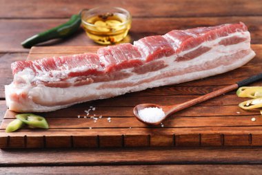 Çiğ domuz göbeği, yeşil biber, ahşap masada baharatlı tuz ve yağ, yakın plan.