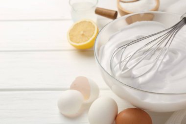 Krem şantili kase, çırpma ve malzemeler beyaz ahşap masada. Metin için boşluk