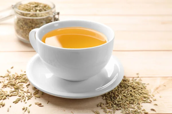 Fennel tea in cup and seeds on light wooden table, closeup