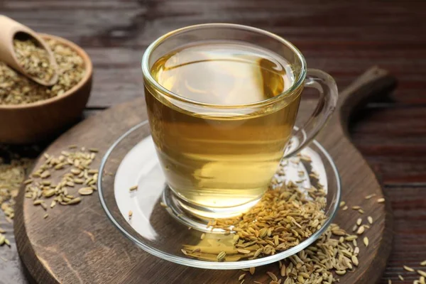 Aromatic fennel tea and seeds on wooden table, closeup
