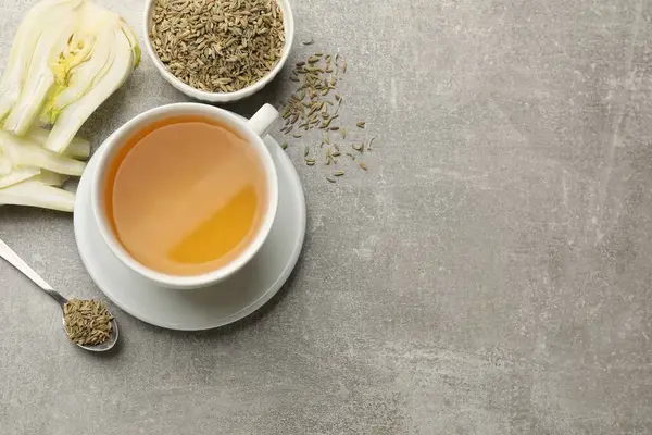 Aromatic fennel tea, seeds and fresh vegetable on grey table, flat lay. Space for text