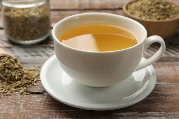 Aromatic fennel tea in cup and seeds on wooden table, closeup