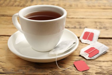 Çay poşetleri ve bir fincan sıcak içecek ahşap masada, yakın plan.