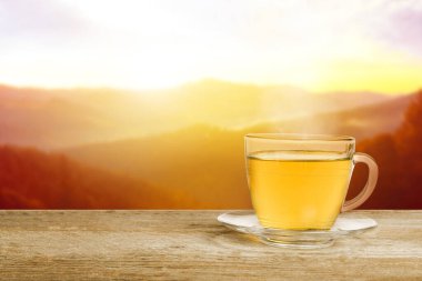 Aromatik yeşil çay cam bardakta, ahşap masada güneş doğarken dağlarda, metin için yer var.